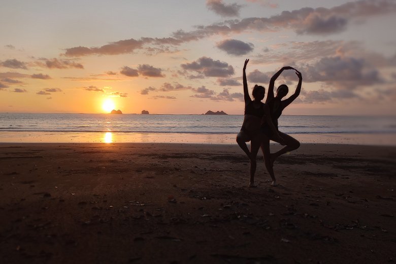 Sunset silhouette of two person doing yoga on the beach at Villas Azul Ballena